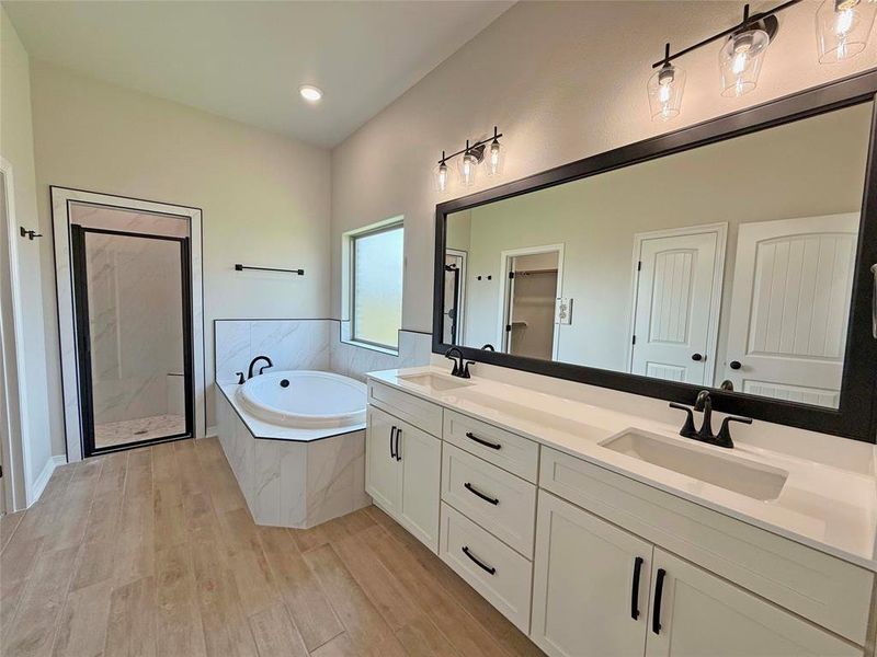Full bath with wood finished floors, a garden tub, a stall shower, and a sink Full bath with wood finished floors, a garden tub, a stall shower, and a sink