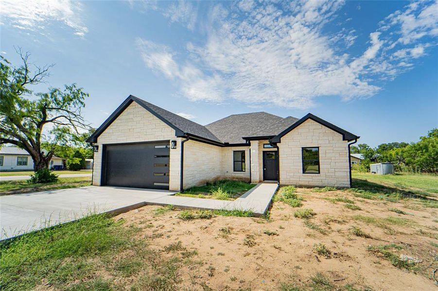 Contemporary exterior featuring light-colored stone veneer, a dark shingle roof, black trim, and a modern garage door with horizontal glass inserts