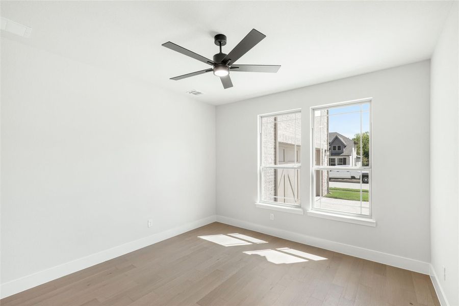 Empty bedroom with hardwood floors, black ceiling fan, and two white-framed windows Empty bedroom with hardwood floors, black ceiling fan, and two white-framed windows