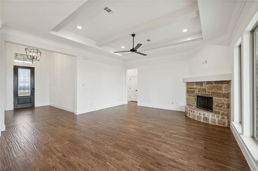 Unfurnished living room with a raised ceiling, dark hardwood / wood-style floors, ceiling fan with notable chandelier, a stone fireplace, and crown molding