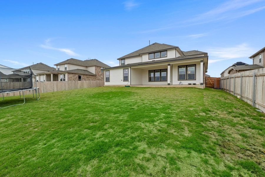 Expansive grassed yard with a two-story residence featuring a covered patio