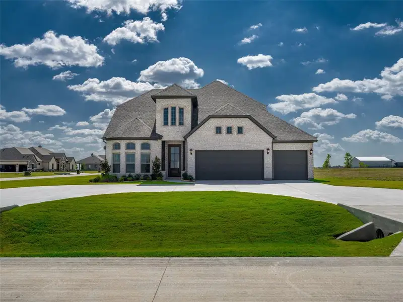 French country inspired facade with brick siding, driveway, roof with shingles, a front yard, and a garage French country inspired facade with brick siding, driveway, roof with shingles, a front yard, and a garage