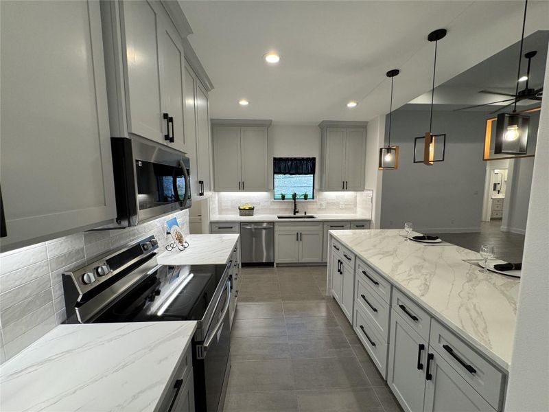 Kitchen featuring stainless steel appliances, tasteful backsplash, recessed lighting, light stone counters, and hanging light fixtures Kitchen featuring stainless steel appliances, tasteful backsplash, recessed lighting, light stone counters, and hanging light fixtures
