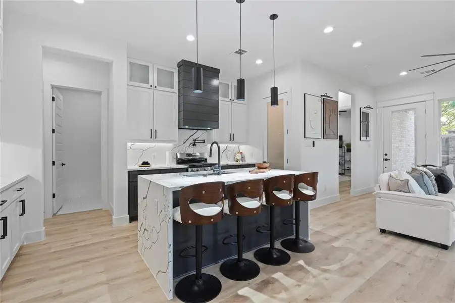 Kitchen with light wood-style flooring, glass insert cabinets, recessed lighting, a center island with sink, and a breakfast bar area