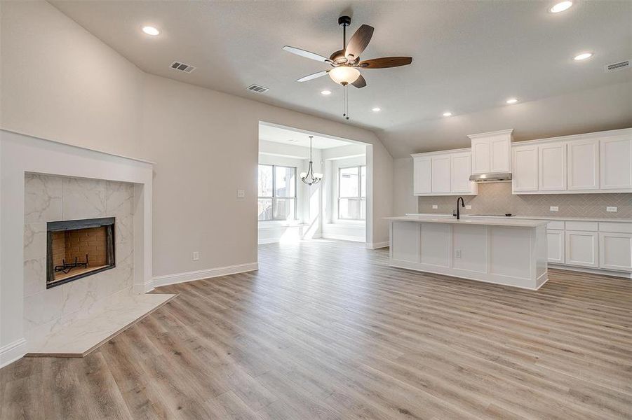 Unfurnished living room with lofted ceiling, a high end fireplace, ceiling fan with notable chandelier, sink, and light hardwood / wood-style floors