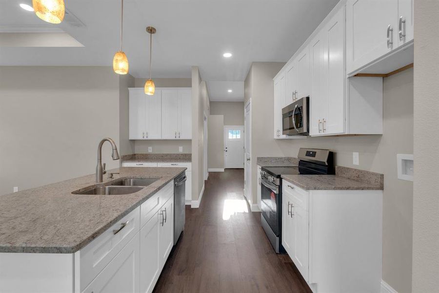 Kitchen featuring stainless steel appliances, dark wood-type flooring, sink, white cabinetry, and decorative light fixtures