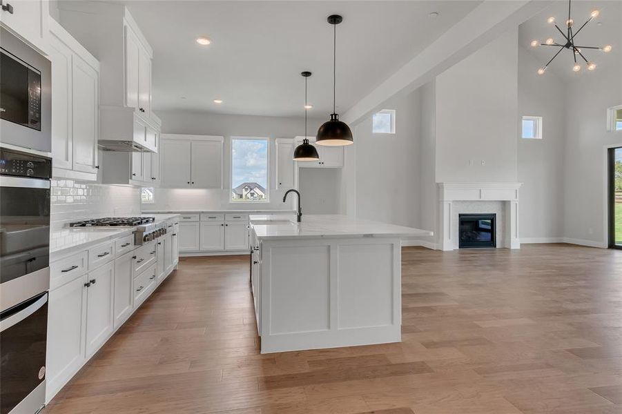 Kitchen with pendant lighting, a kitchen island with sink, white cabinets, light hardwood / wood-style flooring, and appliances with stainless steel finishes