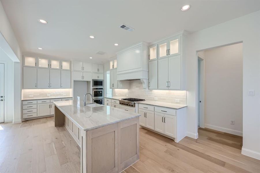 Kitchen with appliances with stainless steel finishes, white cabinets, light wood-type flooring, and an island with sink