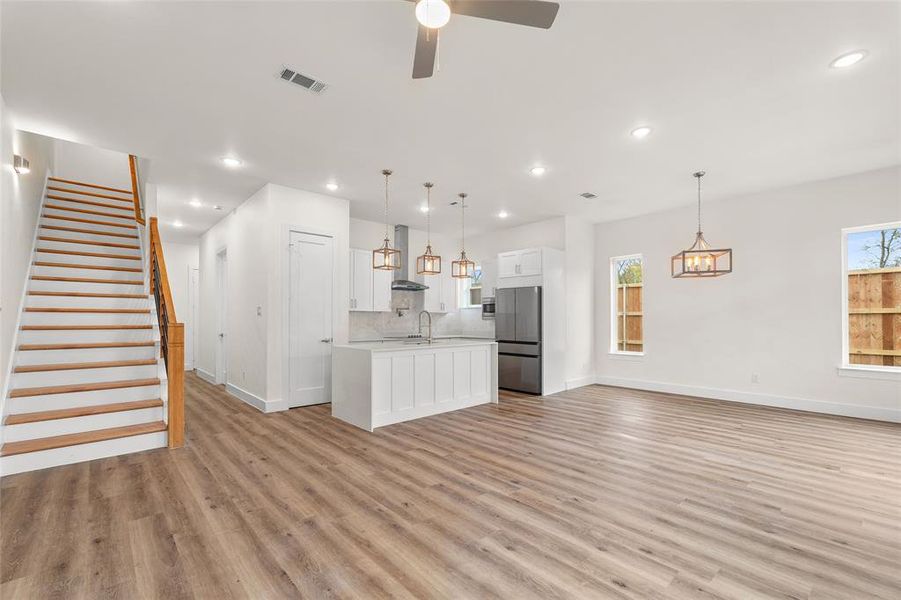 Kitchen featuring open floor plan, a kitchen island with sink, white cabinetry, freestanding refrigerator, and pendant lighting Kitchen featuring open floor plan, a kitchen island with sink, white cabinetry, freestanding refrigerator, and pendant lighting