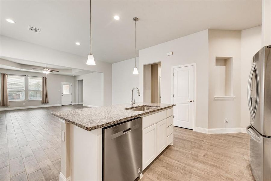 Kitchen featuring appliances with stainless steel finishes, light stone counters, light wood-style flooring, decorative light fixtures, and recessed lighting