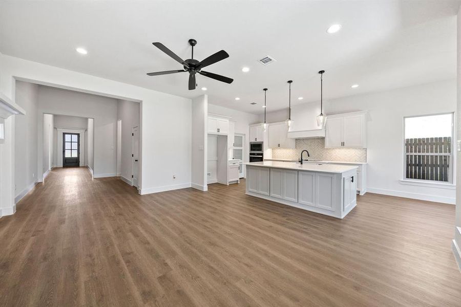 Kitchen with white cabinetry, a center island with sink, open floor plan, and a ceiling fan