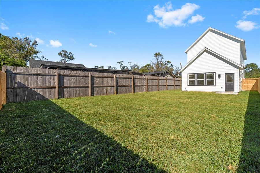 From the backyard, enjoy the full view of the spacious yard and the home’s striking design, featuring white siding, black window trim, and a sleek black back door. (Photo may be enhanced and may include virtual staging)