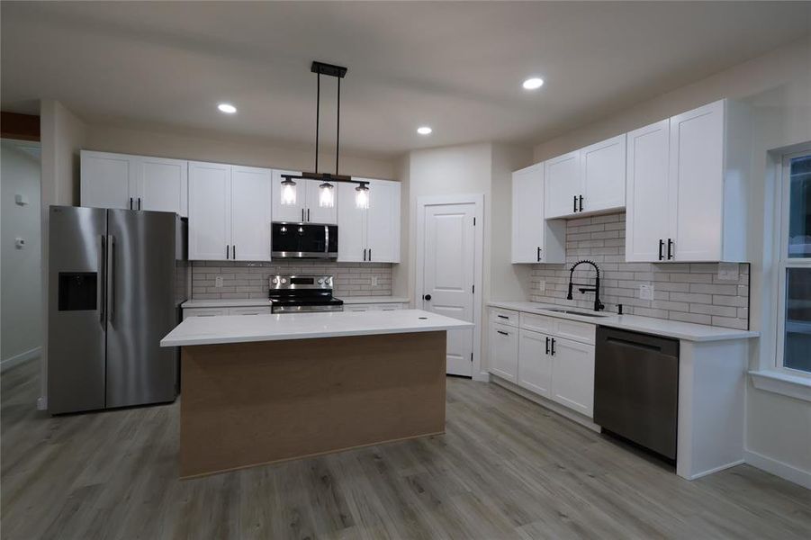 Kitchen featuring appliances with stainless steel finishes, a center island, white cabinets, hanging light fixtures, and light wood-style flooring