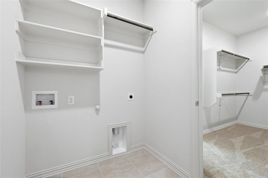 Dedicated utility area with tiled flooring, integrated shelving, and clothing rod