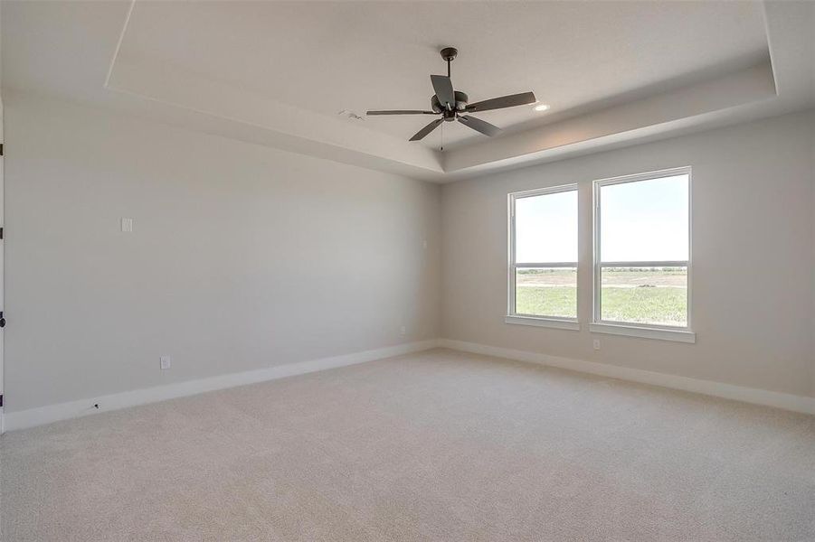 Spare room featuring a tray ceiling, baseboards, ceiling fan, and light carpet Spare room featuring a tray ceiling, baseboards, ceiling fan, and light carpet