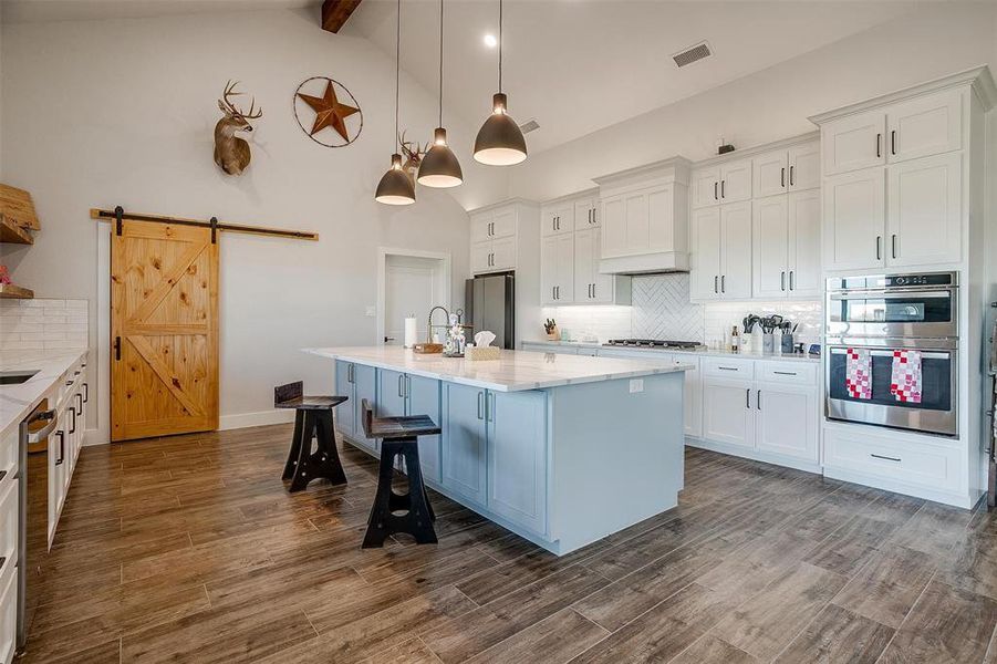 Kitchen with white cabinetry, beamed ceiling, stainless steel appliances, a barn door, and decorative backsplash