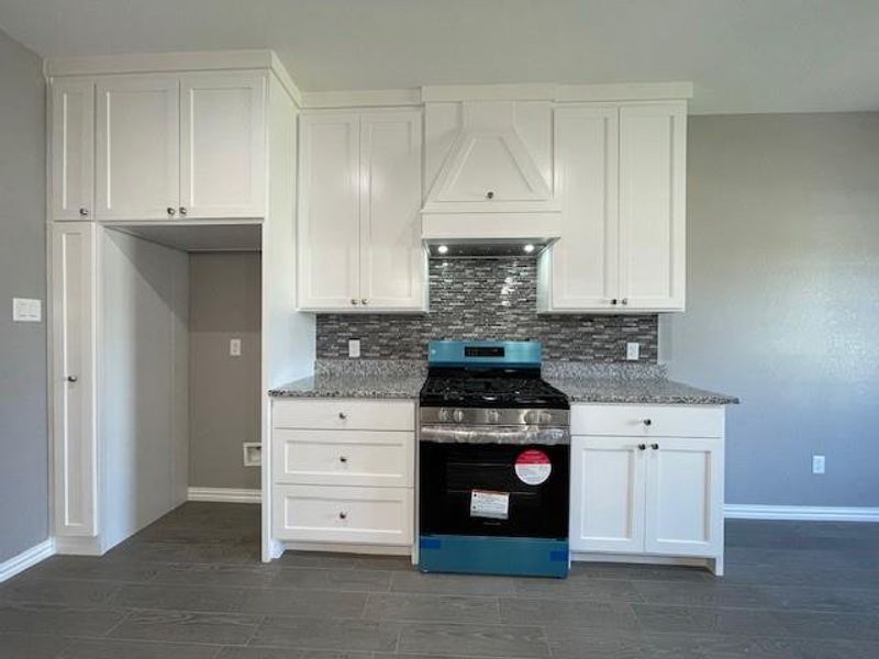 Kitchen with stainless steel gas stove, tasteful backsplash, custom exhaust hood, and white cabinetry Kitchen with stainless steel gas stove, tasteful backsplash, custom exhaust hood, and white cabinetry
