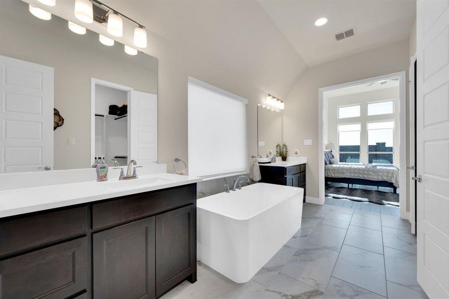 Gorgeous upgraded soaking free standing tub divides the separate vanities with a privacy roller shade over window.