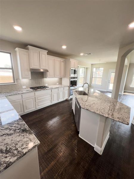 Kitchen with tasteful backsplash, appliances with stainless steel finishes, sink, white cabinetry, and a kitchen island with sink