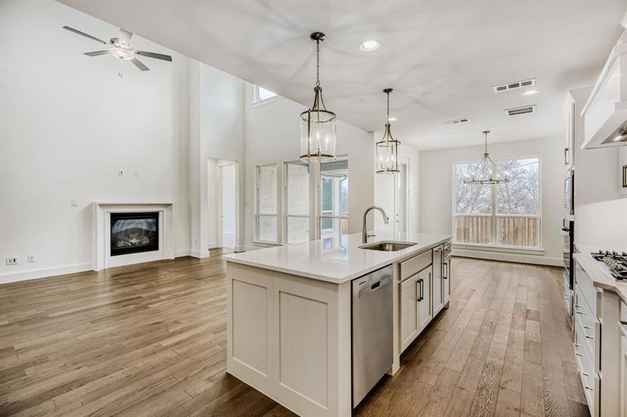 Kitchen with white cabinets, open floor plan, a center island with sink, stainless steel appliances, and hanging lights