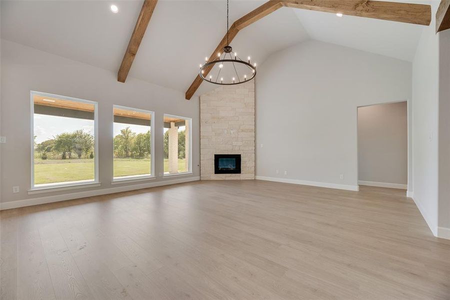Unfurnished living room featuring high vaulted ceiling, light wood-type flooring, a chandelier, beam ceiling, and a stone fireplace