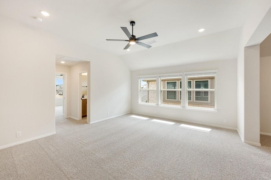Spacious empty bedroom with carpet, ceiling fan, vaulted ceiling, and three windows overlooking neighboring homes Spacious empty bedroom with carpet, ceiling fan, vaulted ceiling, and three windows overlooking neighboring homes