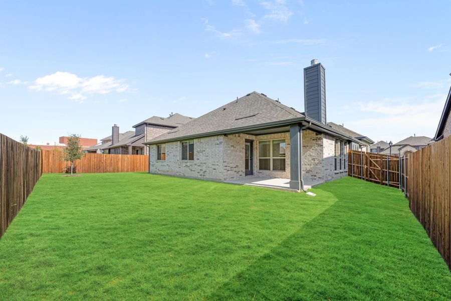 Brick home rear exterior with covered patio, chimney, and fenced backyard with green lawn