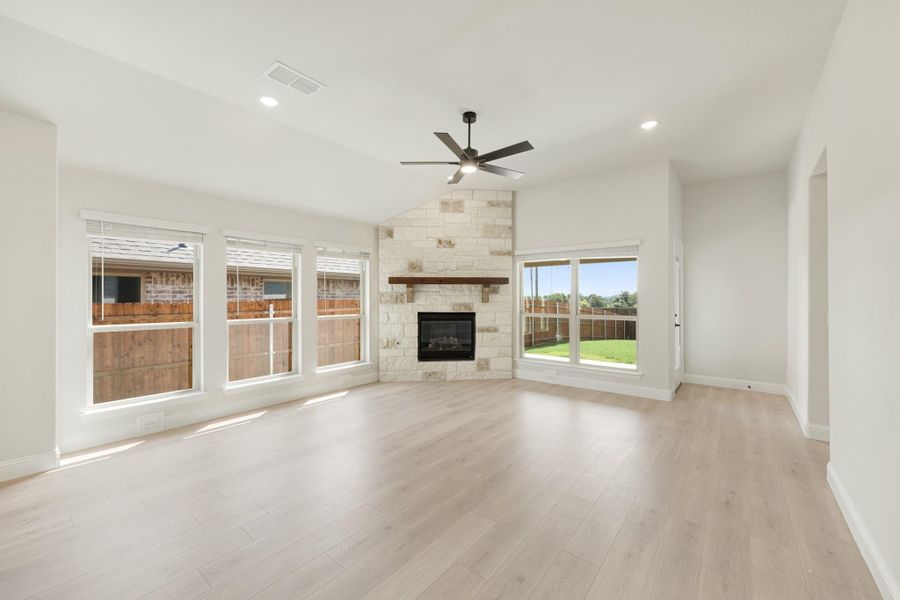 Open living room with stone fireplace, wood mantel, ceiling fan, and light hardwood floors
