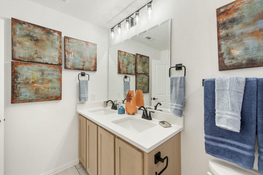 Bathroom with double sink vanity, tan cabinets, white countertop, and large mirror with overhead lighting Bathroom with double sink vanity, tan cabinets, white countertop, and large mirror with overhead lighting