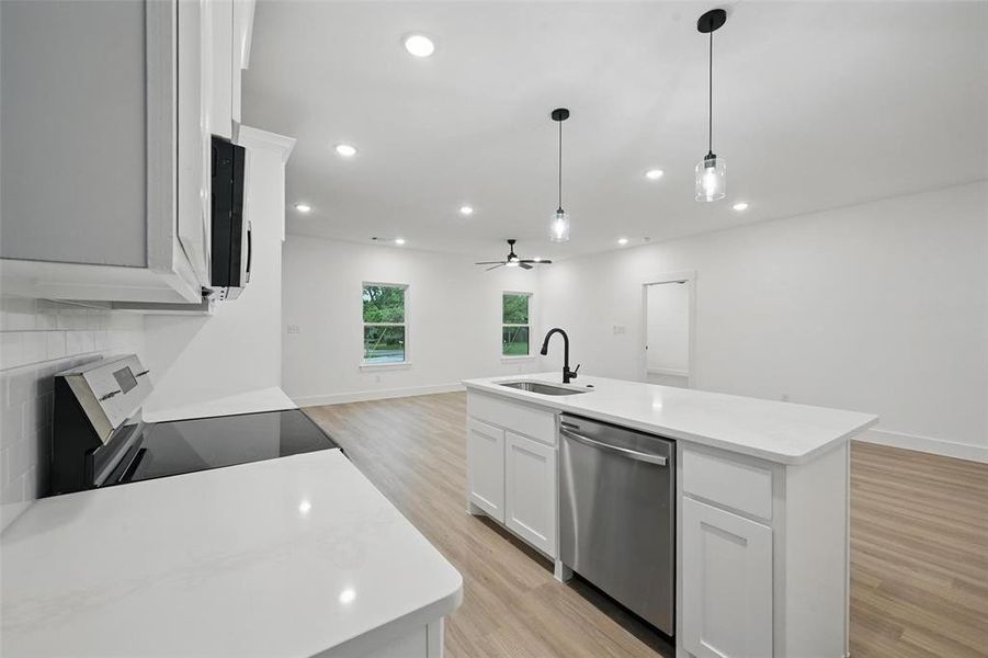 Kitchen with appliances with stainless steel finishes, a sink, open floor plan, light wood-style flooring, and a center island with sink