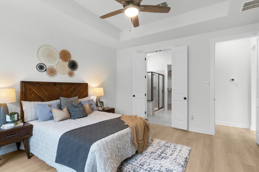 Bedroom featuring a tray ceiling, light wood-type flooring, baseboards, and ceiling fan