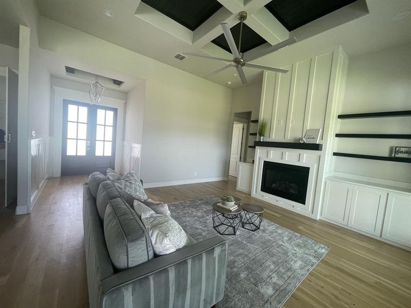 Living area featuring coffered ceiling, light wood-type flooring, ceiling fan, beamed ceiling, and a large fireplace Living area featuring coffered ceiling, light wood-type flooring, ceiling fan, beamed ceiling, and a large fireplace