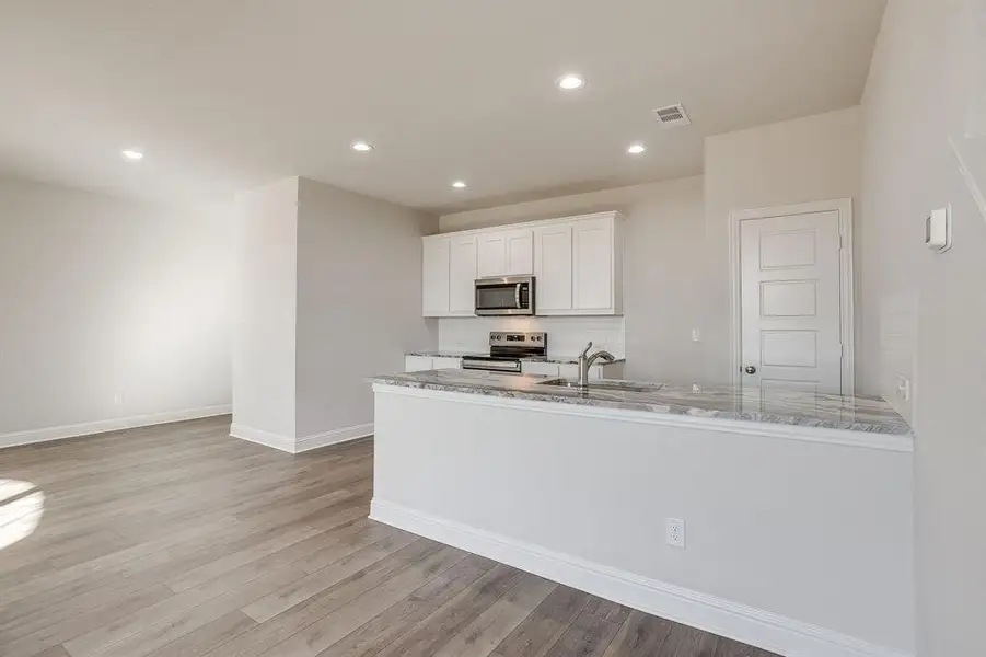 Kitchen featuring white cabinets, light stone counters, stainless steel appliances, light wood-type flooring, and recessed lighting