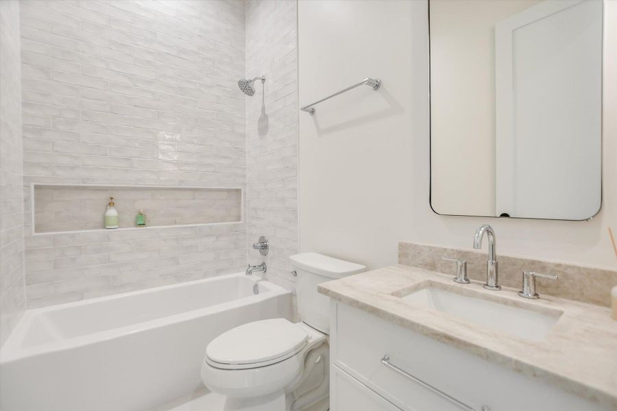 Bathroom featuring a white subway tile surround, integrated shower niche, built-in bathtub, and a vanity with a light-toned stone countertop