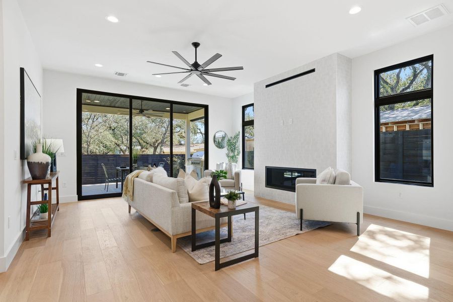 Living area featuring light wood-style floors, a large fireplace, ceiling fan, and recessed lighting