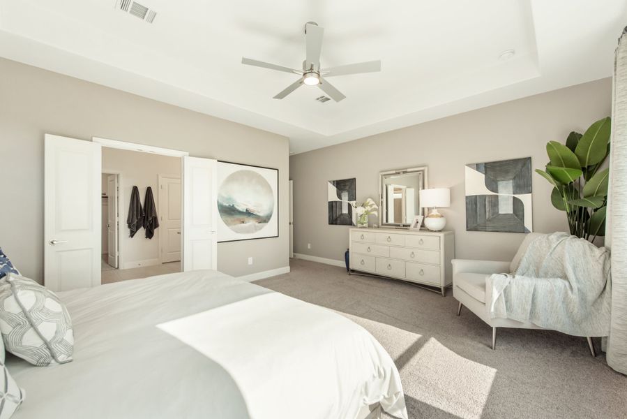 Spacious master bedroom with ceiling fan, carpet flooring, white dresser, and open doors to walk-in closet and bathroom.