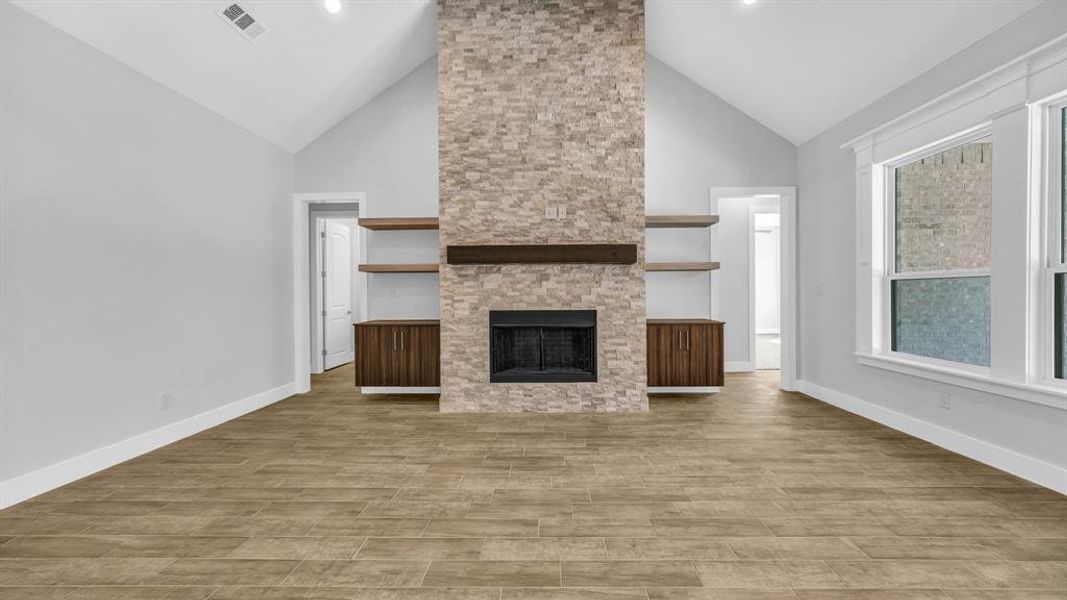 Unfurnished living room featuring beamed ceiling, a stone fireplace, and light hardwood / wood-style floors