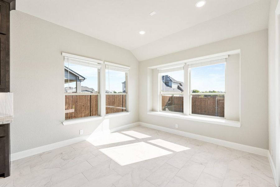 Empty room with vaulted ceiling, marble tile floors, and four large windows with backyard views