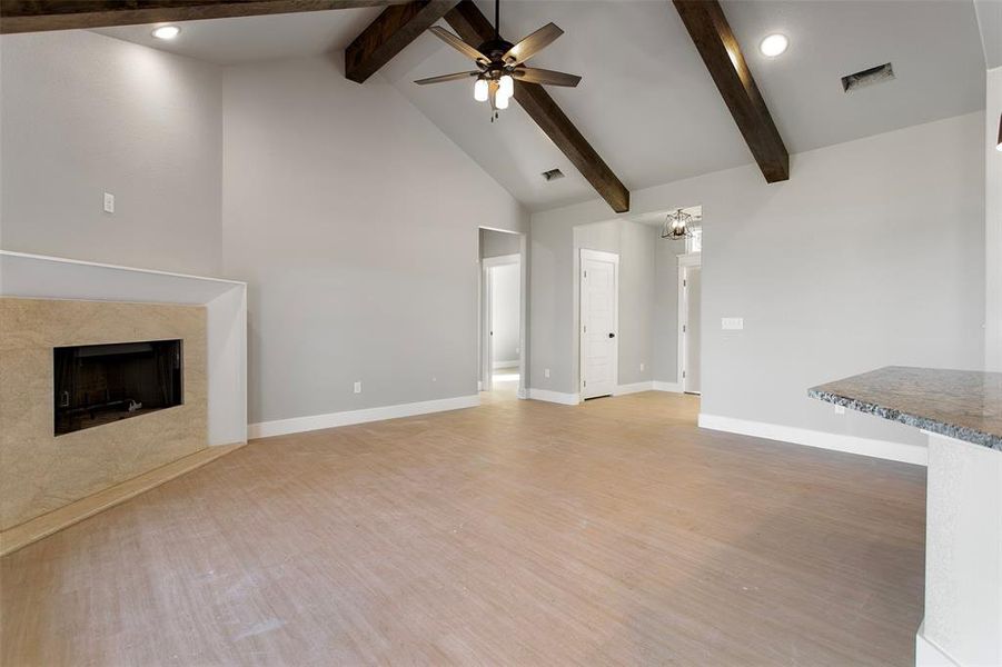 Unfurnished living room featuring beamed ceiling, hardwood / wood-style flooring, a fireplace, and ceiling fan