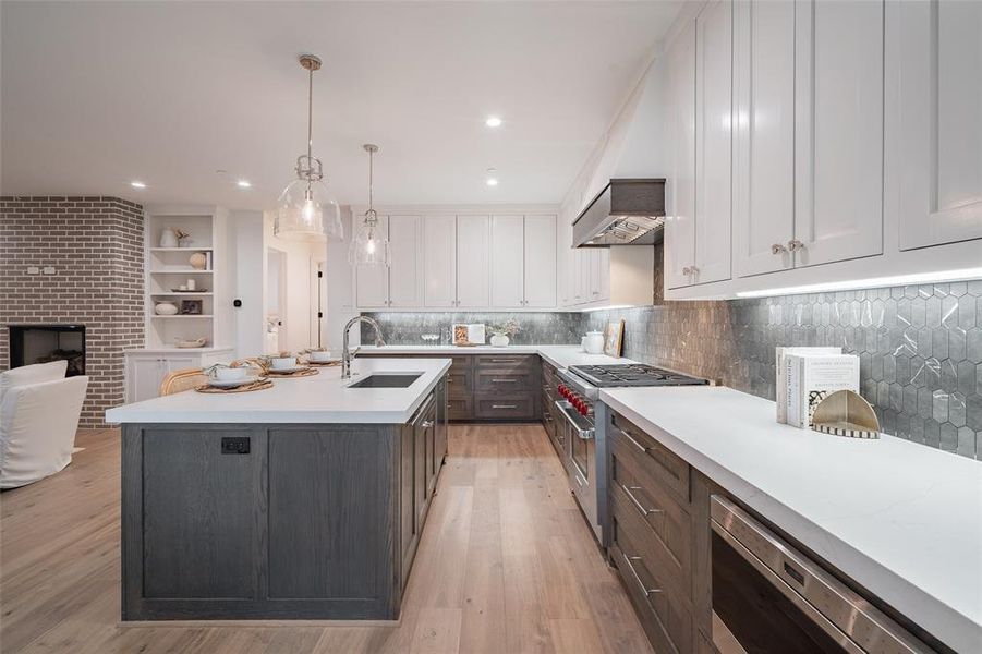 Kitchen featuring sink, high end range, hanging light fixtures, tasteful backsplash, and white cabinets