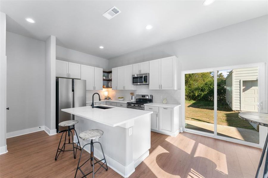 Kitchen with tasteful backsplash, white cabinets, stainless steel appliances, a center island with sink, and a breakfast bar area