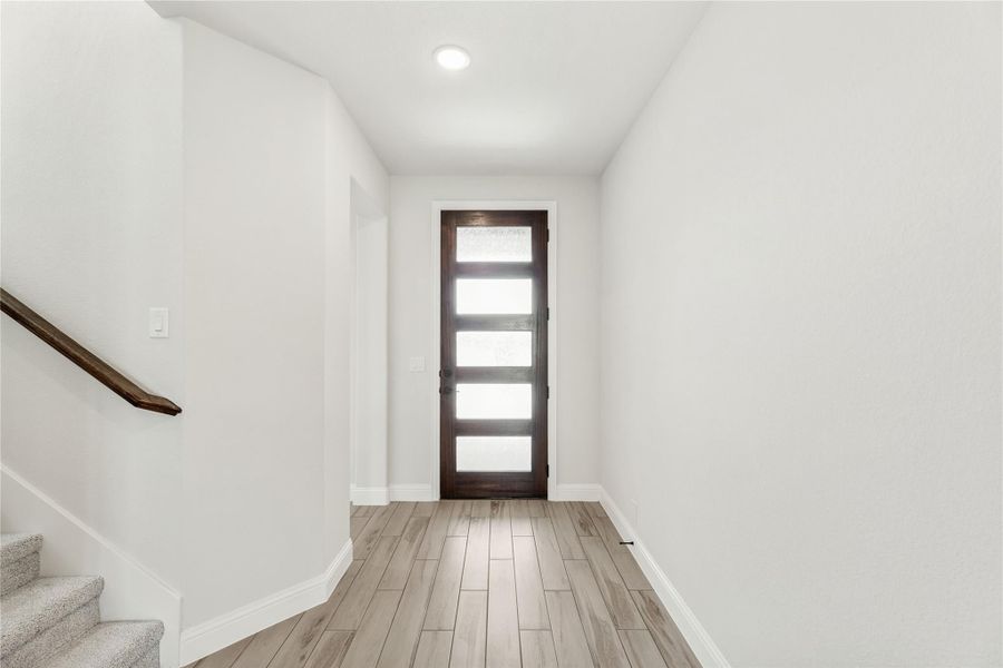 Entryway with dark wood glass-panel front door, light wood floors, and staircase with wood railing