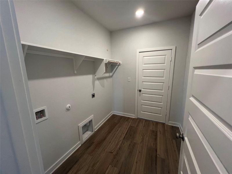 A dedicated laundry room with ample shelving for storage and a durable wood floor.