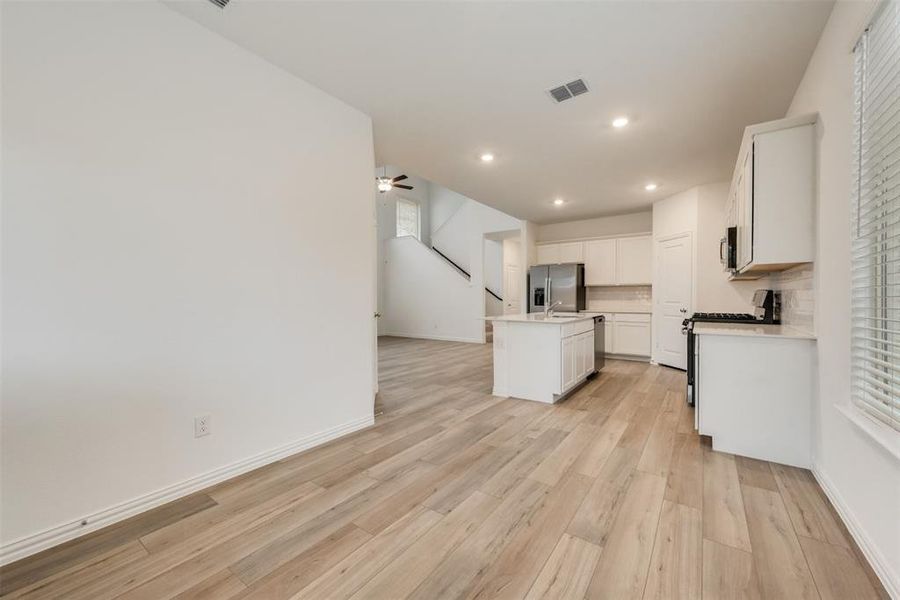 Kitchen featuring a center island with sink, stainless steel appliances, ceiling fan, light wood-type flooring, and white cabinets