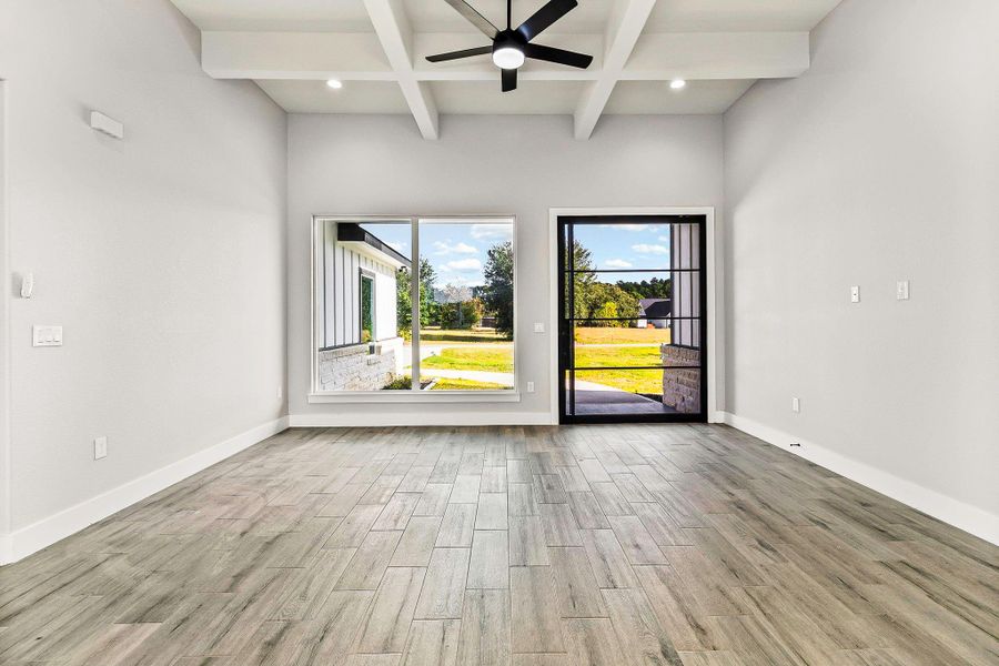This bright room features wood-look tile flooring, a large window with scenic views, and a glass door leading to an outdoor area. The high ceiling with exposed beams and a ceiling fan adds a modern touch. This bright room features wood-look tile flooring, a large window with scenic views, and a glass door leading to an outdoor area. The high ceiling with exposed beams and a ceiling fan adds a modern touch.
