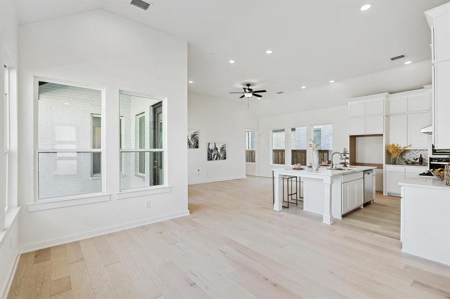 Kitchen featuring a center island with sink, sink, vaulted ceiling, light hardwood / wood-style floors, and white cabinetry