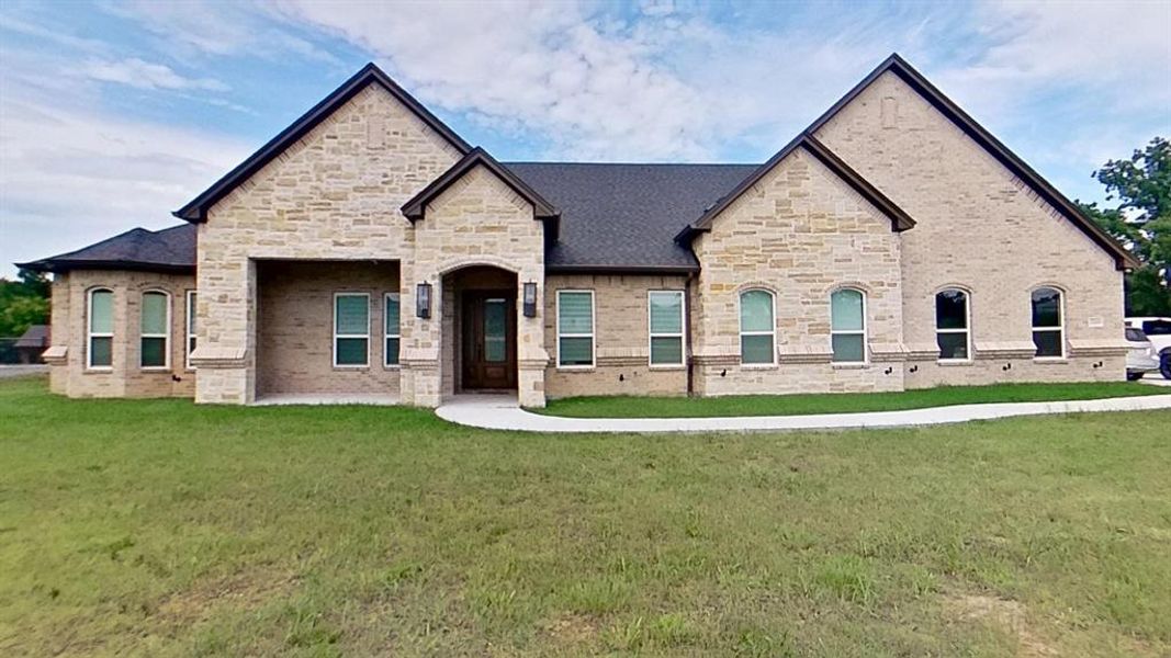 Stone and brick facade featuring a covered entry, arched doorway with glass paneling, and a dark shingle roof Stone and brick facade featuring a covered entry, arched doorway with glass paneling, and a dark shingle roof