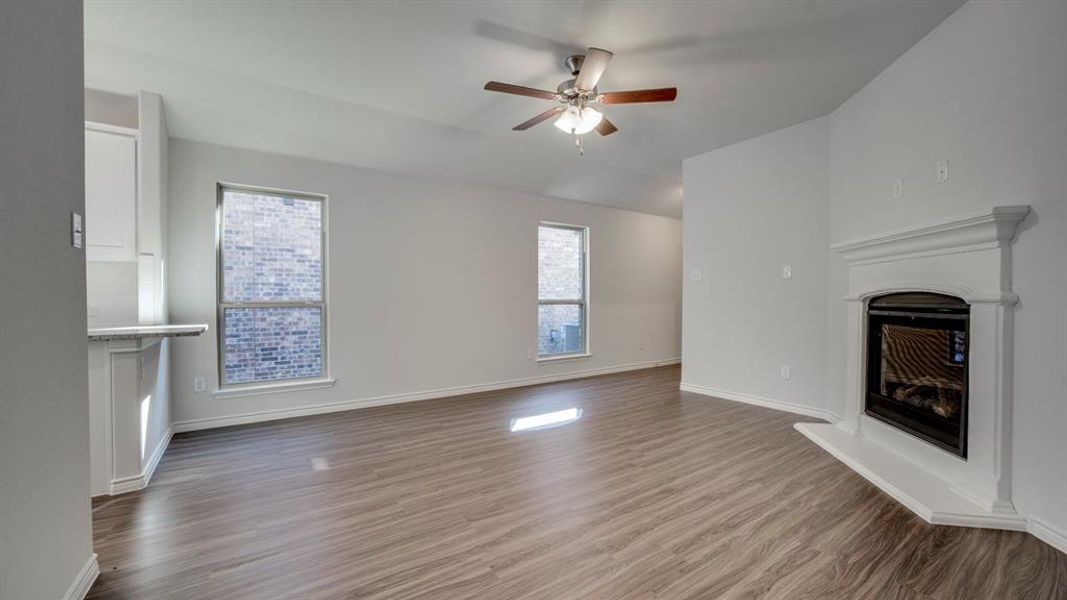 Unfurnished living room with a glass covered fireplace, a ceiling fan, and dark wood-style flooring