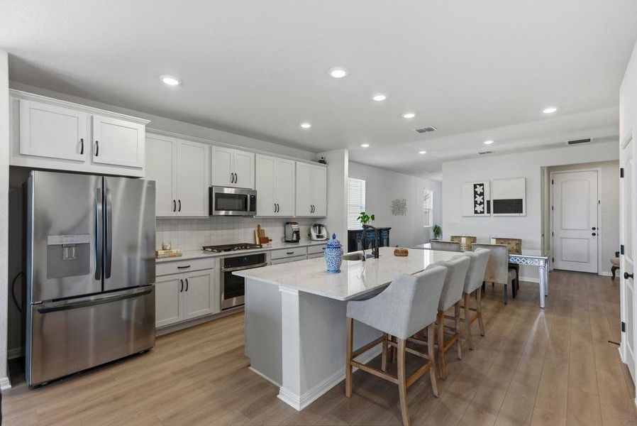 Kitchen featuring appliances with stainless steel finishes, light stone countertops, a breakfast bar area, light wood-style flooring, and an island with sink