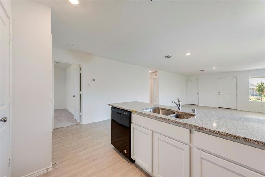 Kitchen with light wood-type flooring, white cabinets, dishwasher, light stone counters, and sink